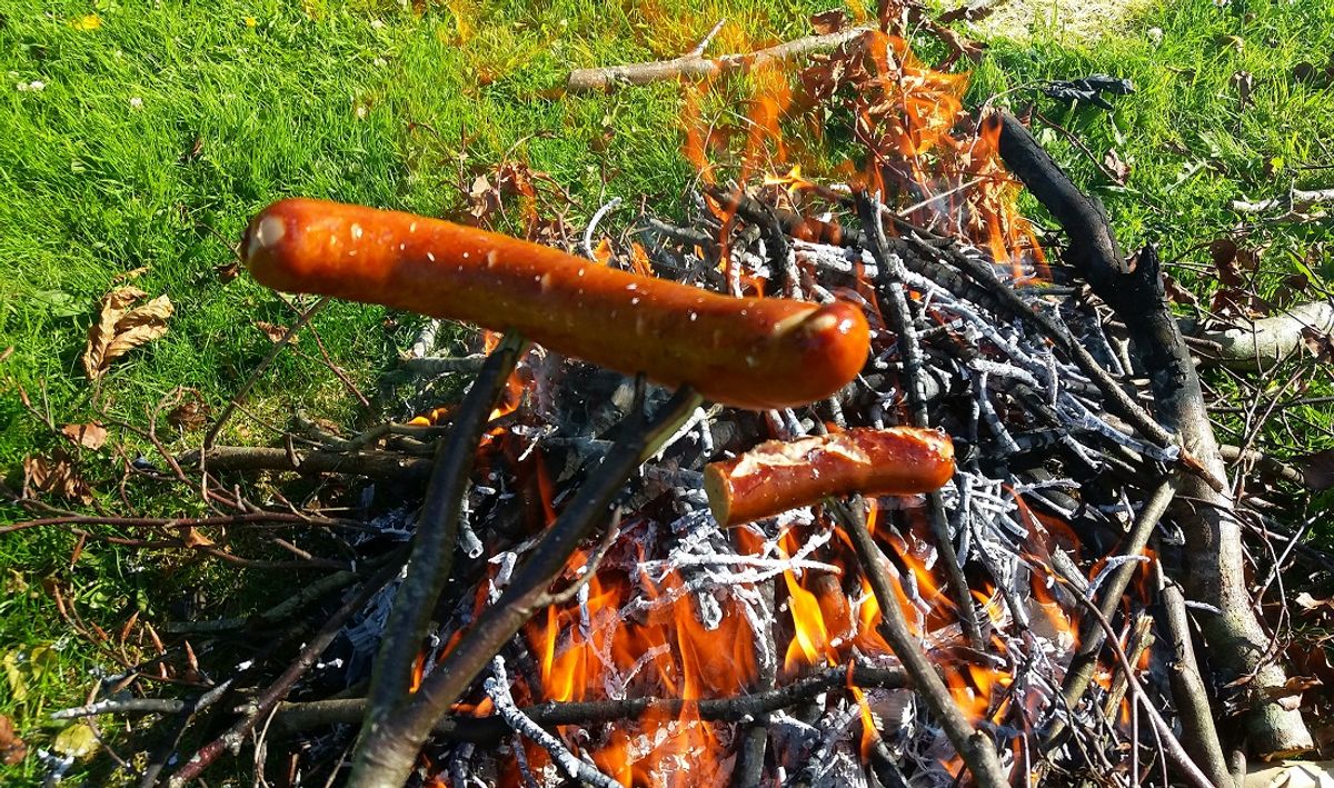 Grilling sausages over a an open campfire fire outdoors (mikroman6 / Getty Images)