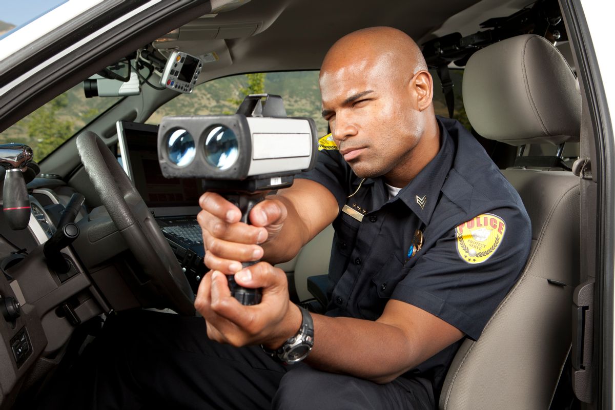 Police Officer checking vehicle speed with radar gun. This stock image has a horizontal composition. Arm Badge Create by me, Gold Chest Emblem Custom Ordered Generic (Getty Images)