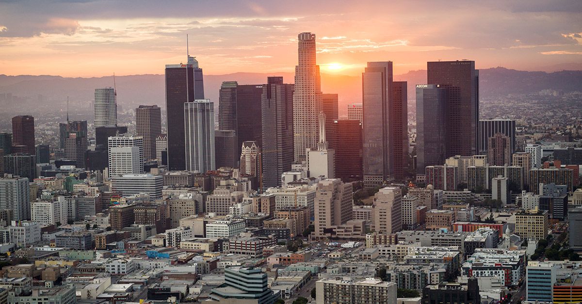 Aerial looking at Downtown Los Angeles, facing west towards the sun setting behind the mountains in the distance, camera wide on the buildings and skyscrapers, beautiful end of the day sunset with sun rays of light in LA, California USA (Nisian Hughes) (Nisian Hughes)