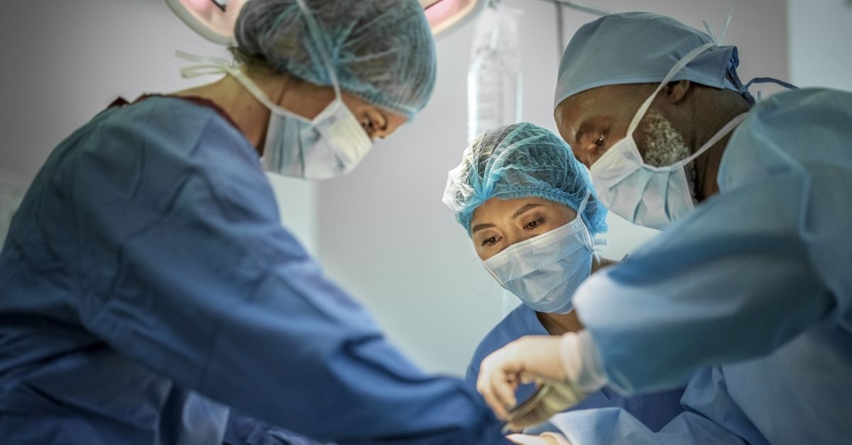 Team of doctors are performing surgery on a patient at hospital. Multi-ethnic surgeons are operating patient in emergency room. They are wearing blue scrubs. (HRAUN/Getty Images)