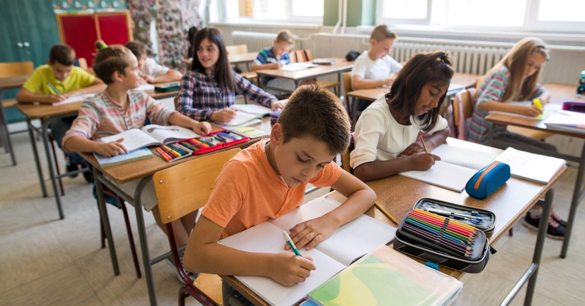 Large group of elementary students learning in the classroom. Focus is on schoolboy writing in workbook. (Getty Images/Stock photo)