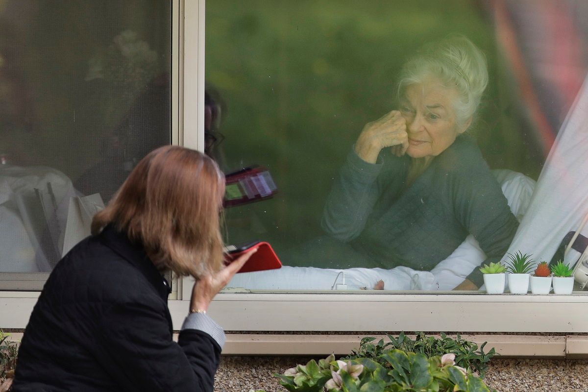 Judie Shape, right, who has tested positive for the new coronavirus, but isn't showing symptoms, smiles as she visits through the window and on the phone with her daughter Lori Spencer, left, Tuesday, March 17, 2020, at the Life Care Center in Kirkland, Wash., near Seattle. In-person visits are not allowed at the nursing home, which is at the center of the outbreak of the new coronavirus in the United States. (AP Photo/Ted S. Warren) (AP Photo / Ted S. Warren)