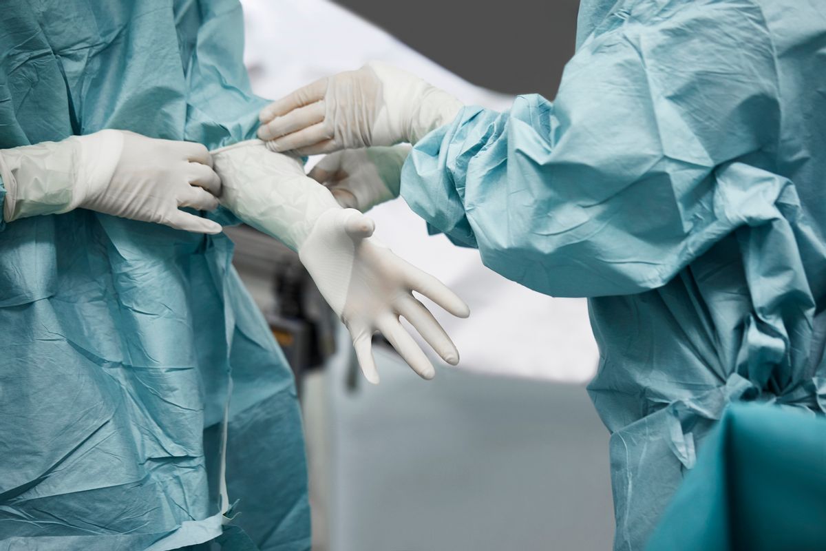 Midsection of female doctor helping surgeon wearing surgical glove. Medical colleagues are preparing for surgery. They are standing in emergency room. (Getty Images/Stock photo)