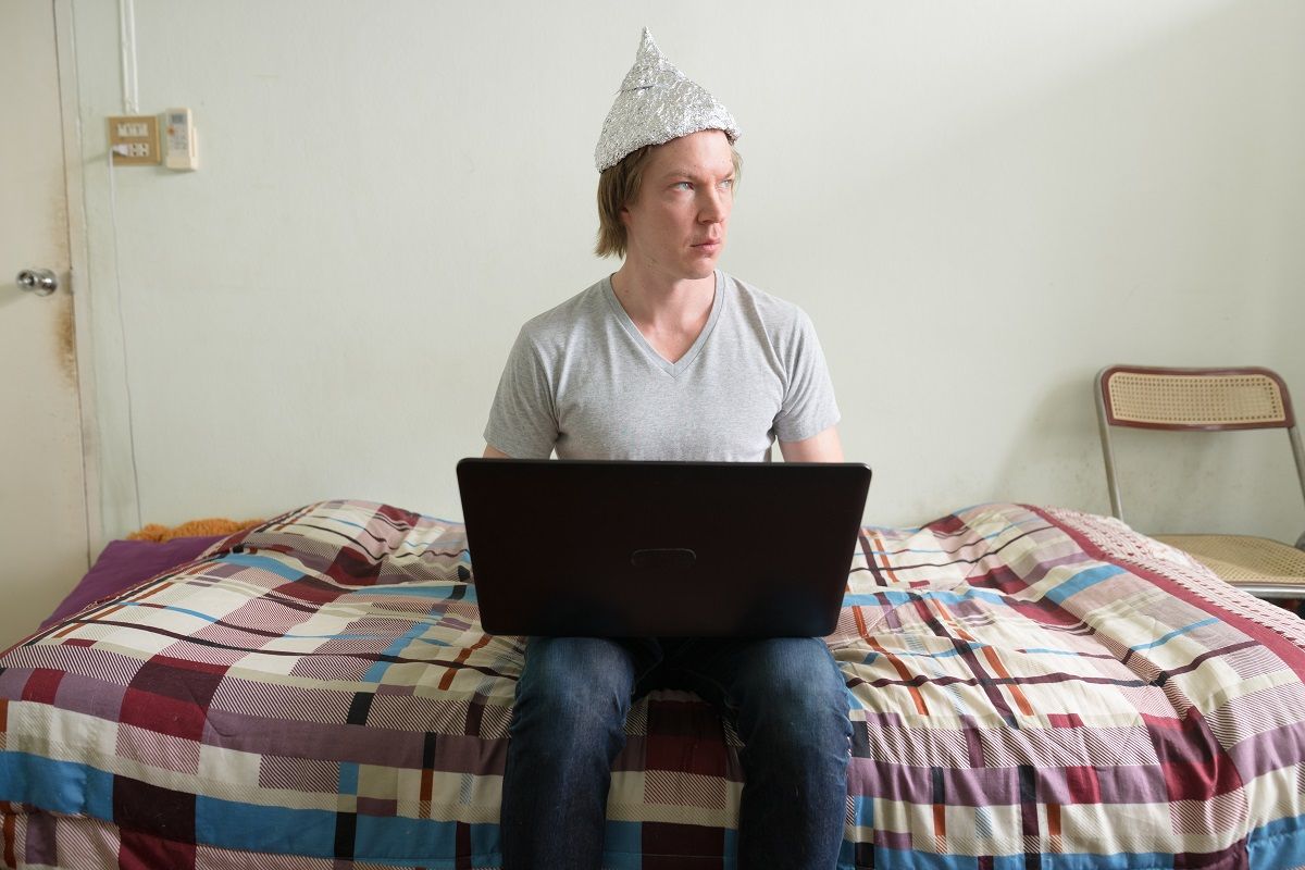 Portrait of young handsome man wearing tin foil hat as conspiracy theory concept in the bedroom at home (Getty Images)