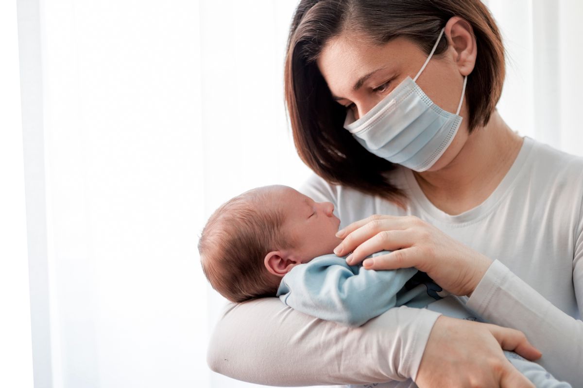 Mother with protective mask holding her baby (Getty Images, stock)