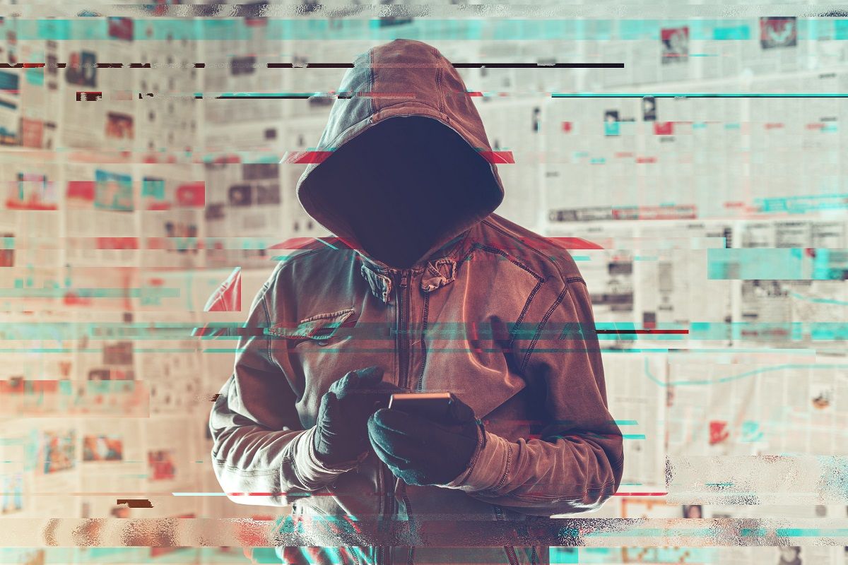 Hooded hacker person using smartphone in infodemic concept with digital glitch effect (stevanovicigor / iStock via Getty Images)
