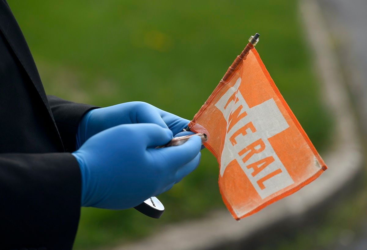 Luis Fernandez, an employee at Stitzel Family Funeral Homes, wearing a mask and gloves, holds a magnetic orange "Funeral" flag to go on the roofs of cars driving to the gravesite . At the Stitzel Family Funeral Home on Kutztown Road in Muhlneberg Thursday afternoon April 16, 2020 where the funeral for Tom Minh Nguyen was being held as a drive-up viewing so that mourners could pay their respects without getting out of their cars and still maintaining social distancing during the Coronavirus / COVID-19 crisis. (Ben Hasty / MediaNews Group/ Reading Eagle via Getty Images)