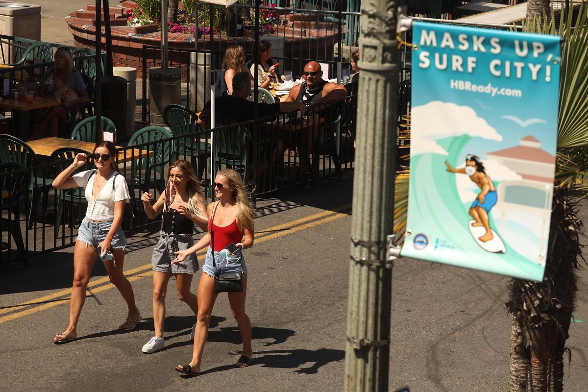 HUNTINGTON BEACH, CA - AUGUST 12, 2020 - - Pedestrians dont heed the, Masks Up, Surf City, banner campaign to prevent coronavirus on Main Street in  Huntington Beach on August 12, 2020. The campaign, a play on the phrase Surfs Up, includes 100 pennants, a banner at the pier and digital displays citywide, Huntington Beach spokeswoman Catherine Jun said. Fifty pennants were installed downtown on Aug. 6. The remaining signs are in production this week, and 13 pennants and a banner are expected to be installed on the Huntington Beach Pier.  (Genaro Molina / Los Angeles Times via Getty Images) (Genaro Molina / Los Angeles Times via Getty Images)