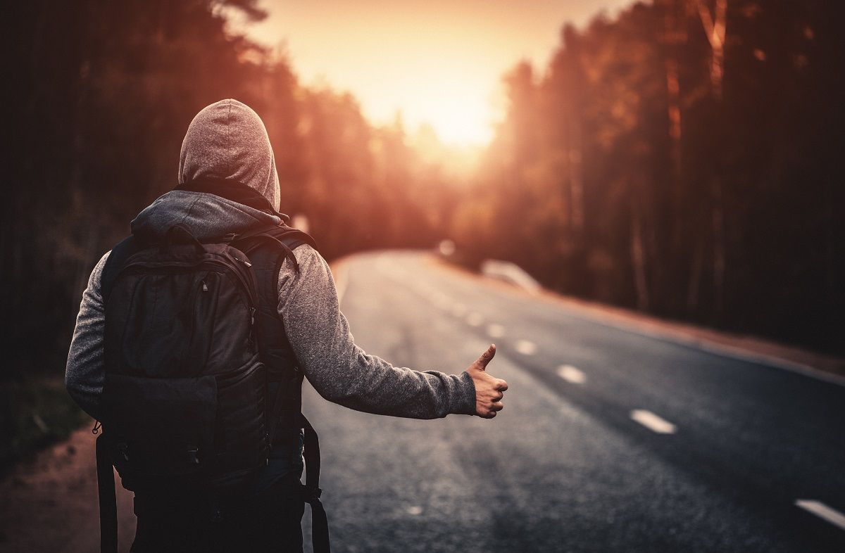 Hitchhiking traveler with backpack trying to stop the car on road in the forest at sunset. Stock photo. (Getty Images /  da-kuk)