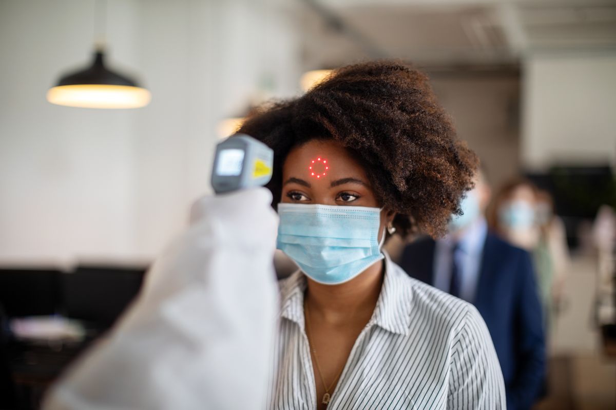 Woman wearing protective mask goes through a temperature checks before going to work in the office. New SOP in office to prevent illness. ( Luis Alvarez / Getty Images)