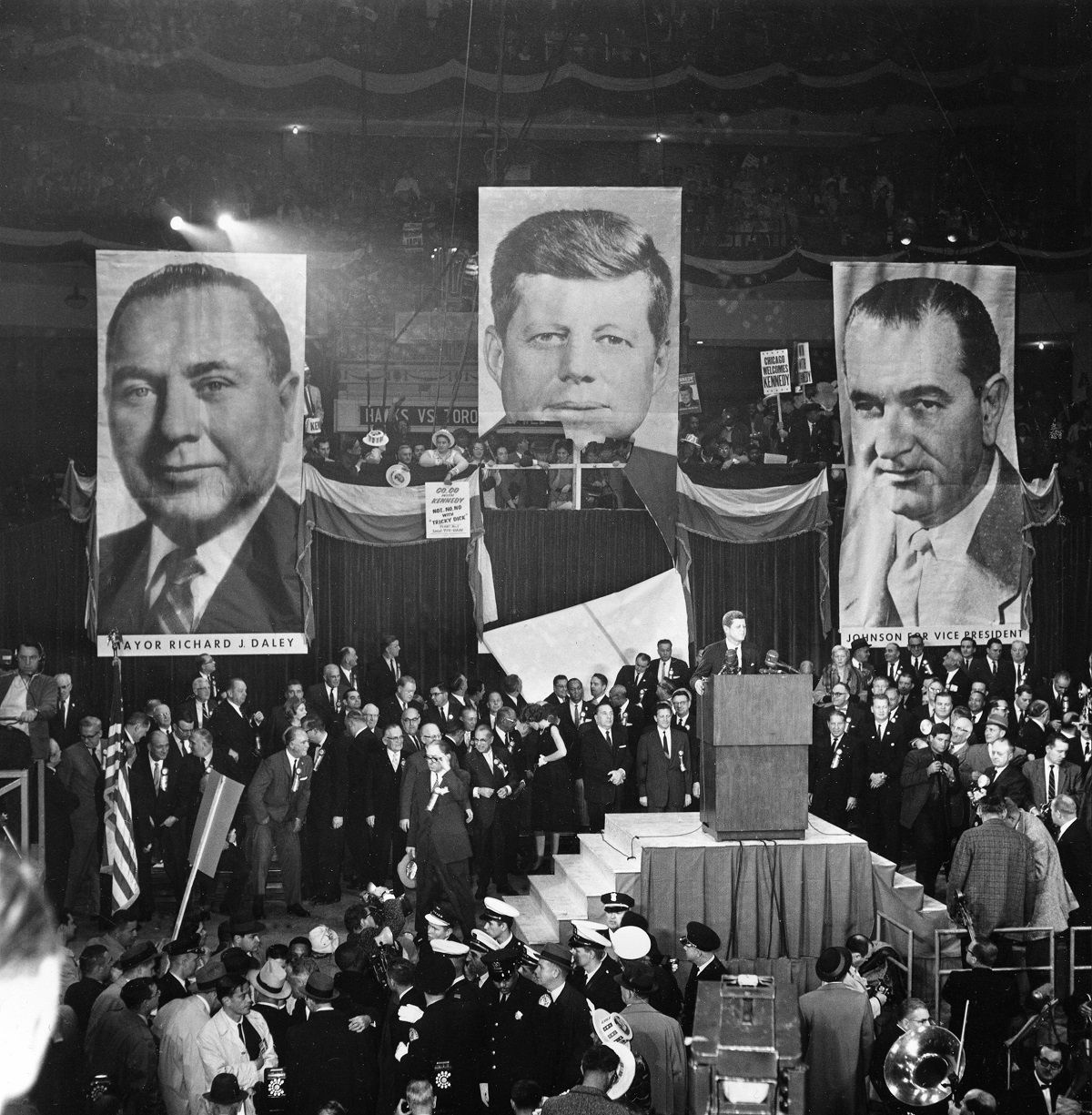 Sen. John F. Kennedy speaks at Chicago Stadium, Ill., Nov. 4, 1960.  Supporters standing on the balcony behind Kennedy have torn away lower half of enlarged picture of the Democratic candidate for president to get a view of the man himself.  Standing on the platform behind Kennedy are his sister, Eunice Shriver, looking back, Chicago Mayor Richard Daley, center, and Otto Kerner, Democratic candidate for Illinois governor. (AP Photo) (AP Photo)