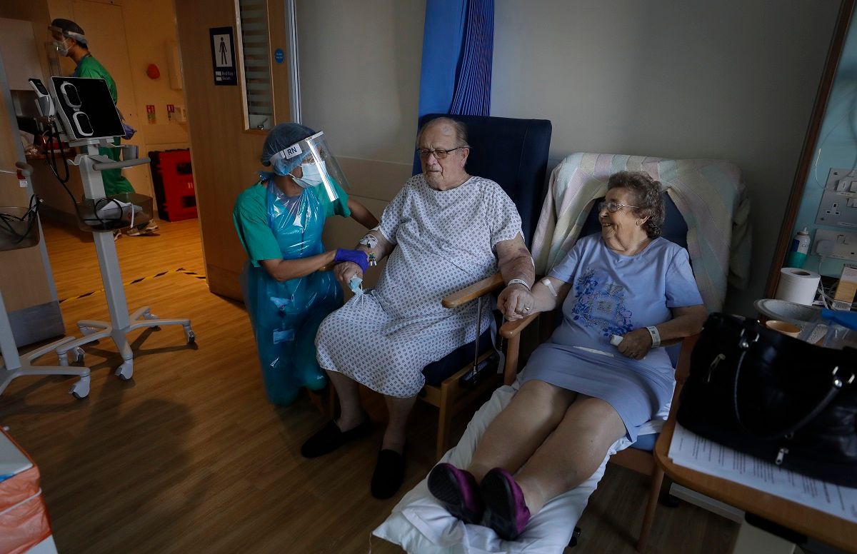 Coronavirus patients George Gilbert, 85 and his wife Domneva Gilbert 84, hold hands during a short visit, they are being treated in different areas, both are part of the TACTIC-R trial, at Addenbrooke's hospital in Cambridge, England, Thursday, May 21, 2020. The new trial known as TACTIC-R is testing whether existing drugs will help prevent the body's immune system from overreacting, which scientists hope could prevent organ failure and death in COVID-19 patients. (AP Photo/Kirsty Wigglesworth, pool) (AP Photo/Kirsty Wigglesworth)
