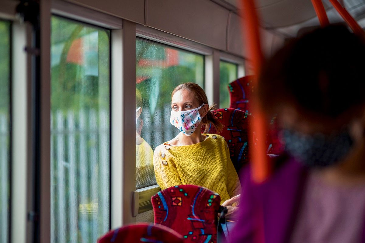 Wide shot of a woman sitting on a public bus wearing a mask, looking out of the window. (SolStock/E+ via Getty Images)