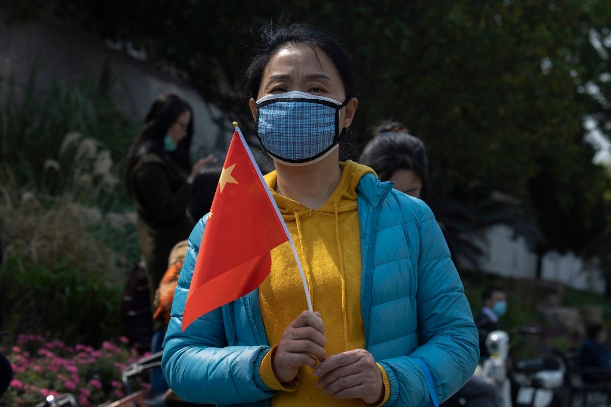 A woman wearing a mask against the new coronavirus holds a Chinese national flag near the site of a national moment of mourning for victims of the coronavirus in Wuhan in central China's Hubei Province, Saturday, April 4, 2020. With air raid sirens wailing and flags at half-staff, China on Saturday held a three-minute nationwide moment of reflection to honor those who have died in the coronavirus outbreak, especially "martyrs" who fell while fighting what has become a global pandemic. (AP Photo/Ng Han Guan)