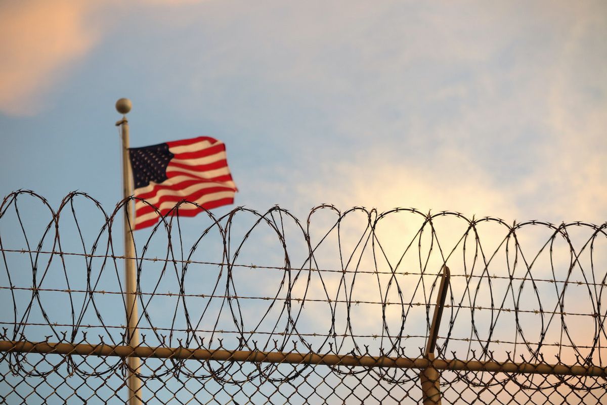 16 October 2018, Cuba, Guantanamo Bay: A US-American flag blows behind a barbed wire fence in the wind. The infamous camp has now existed for almost 17 years. 40 inmates are still being held there. (to dpa "The aging prisoners of Guantánamo Bay" of 27.11.2018) Photo: Maren Hennemuth/dpa (Photo by Maren Hennemuth/picture alliance via Getty Images) (picture alliance / Contributor)