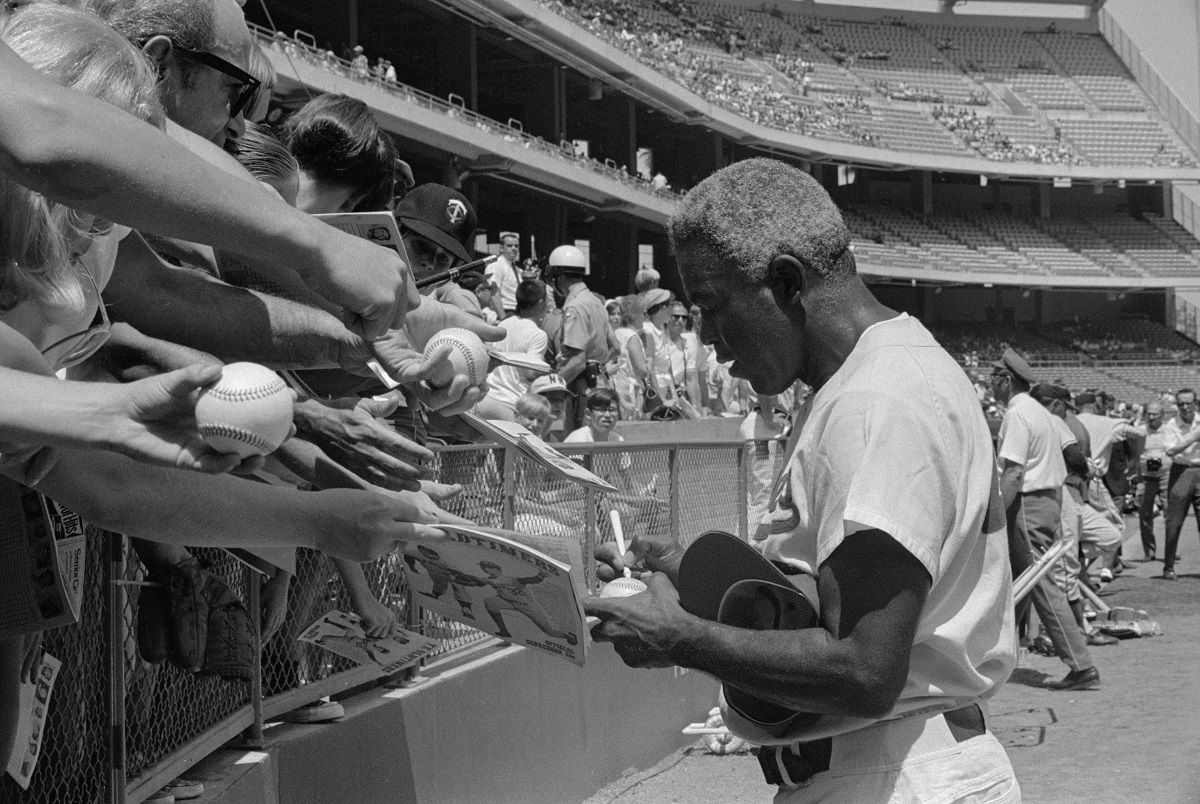 (Original Caption) Former Dodger great Jackie Robinson signs autographs before the start of the "Old timers" game between the Angels-Dodgers at Anaheim Stadium. Robinson was elected to Hall of Fame in 1962, NL's most valuable player in 1949 and was the NL batting champ in 1949. He retired in 1956. (Bettman)