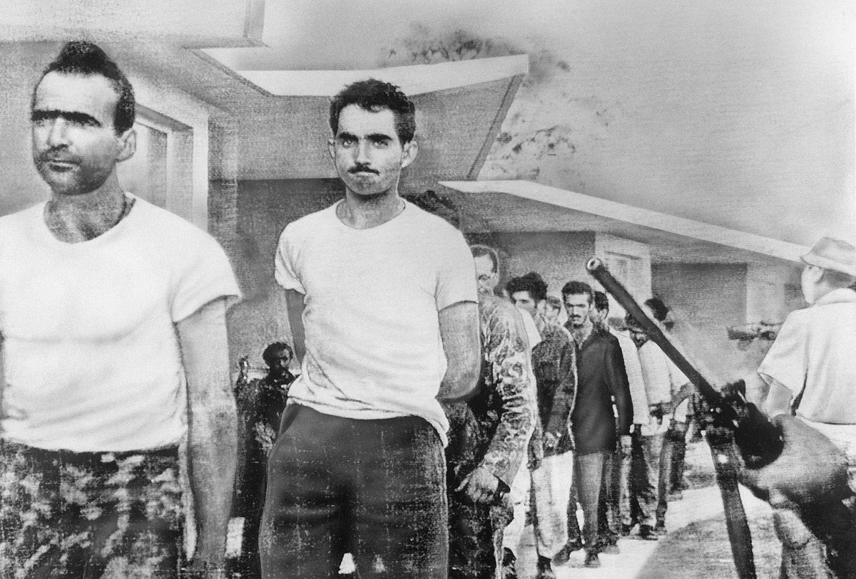 (Original Caption) 4/21/1961-Havana, Cuba- Watched by armed guards, grim-faced invaders are marched off to prison from temporary quarters at Giron Beach, Las Villas province, after their capture by Castro forces. This is one of the first pictures received by Telephoto from United Press International's Havana bureau after restoration of communications. (Bettmann via Getty Images)