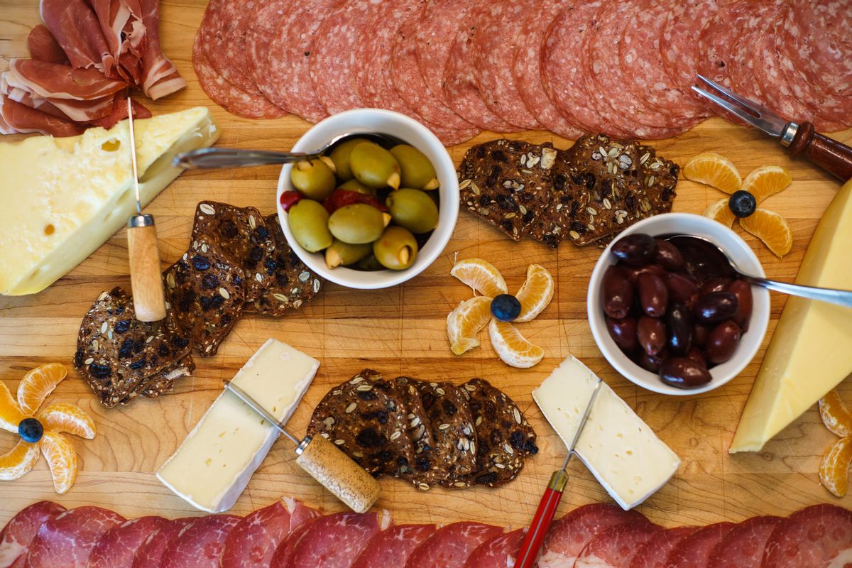 Homemade cheese and charcuterie board, includes crackers, fruit, olives, meat and cheese cutting and serving utensils on large cutting board. Captured with camera positioned directly above subject. Sony a7 and Leica Summicron 35mm at ISO 250 and 1/60th second shutter speed. (Getty Images)