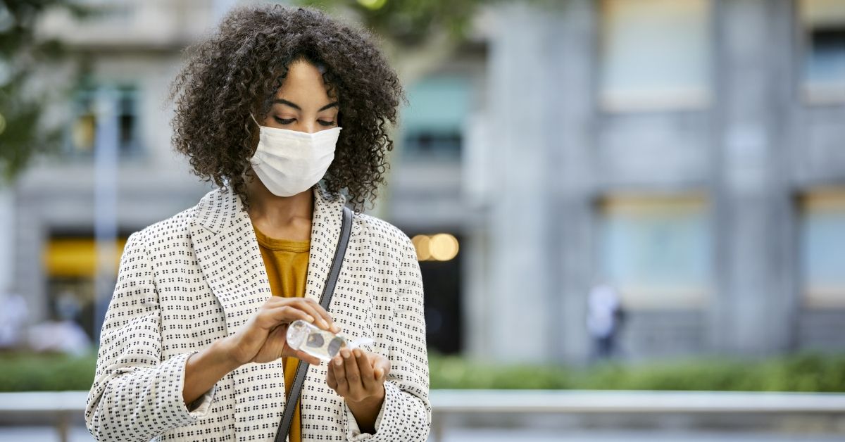 Businesswoman cleaning hand with sanitizer in city. Entrepreneur wearing mask standing outdoors during pandemic. She is in formals. (Getty Images)
