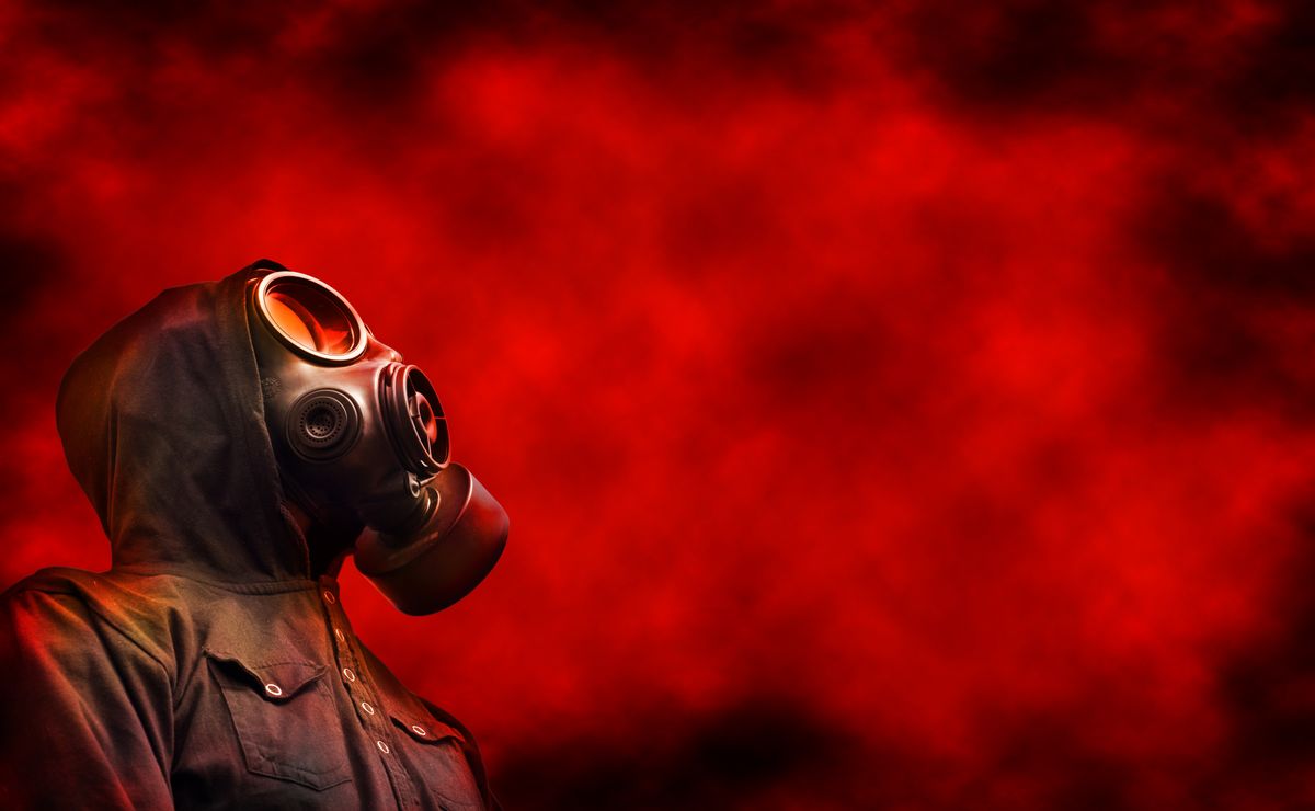 Person wearing hoody and gas mask with red toxic fumes (SEAN GLADWELL / Getty Images)