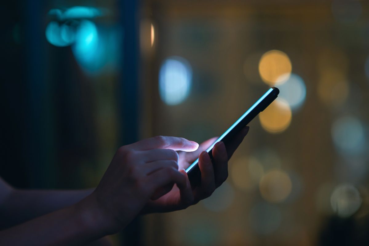 Close up of woman's hand using smartphone in the dark, against illuminated city light bokeh (d3sign / Getty Images)