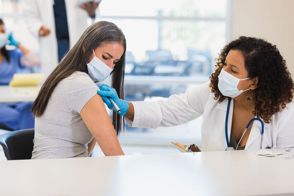 A mid adult female doctor prepares to administer a COVID-19 vaccine or booster dose to a mid adult female patient. The doctor and patient are wearing protective face masks. ( SDI Productions/Getty Images)