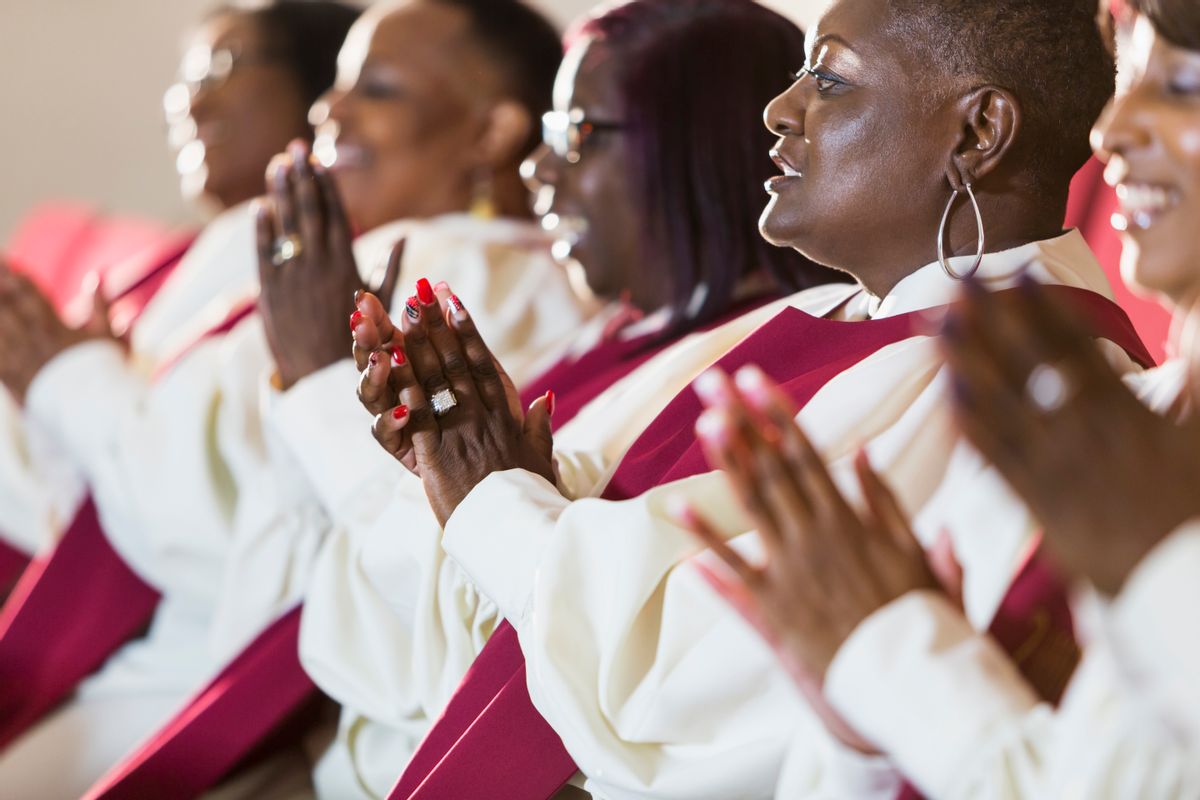 A group of mature black women in church robes, sitting in a row, clapping. They are members of the church choir listening to a sermon. (kali9/Getty Images)