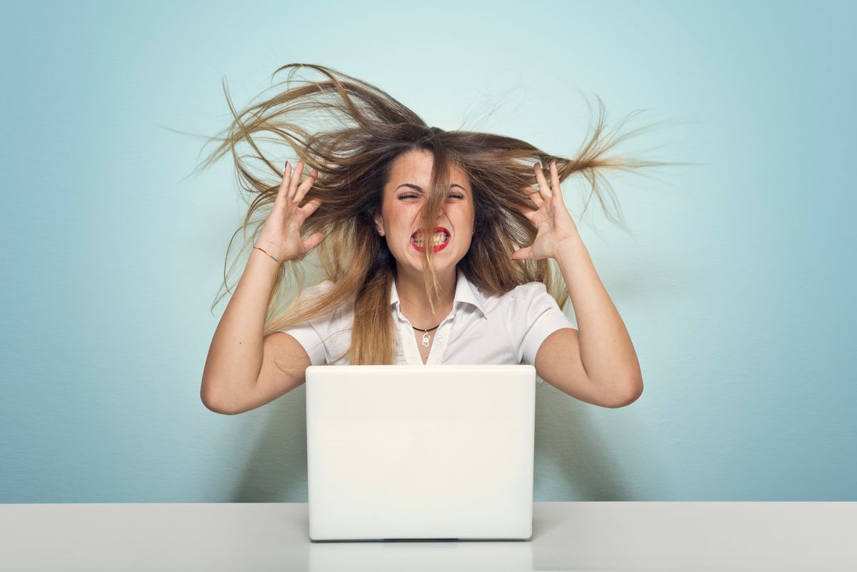 Angry woman screams against her computer.Studio shot (Getty Images)
