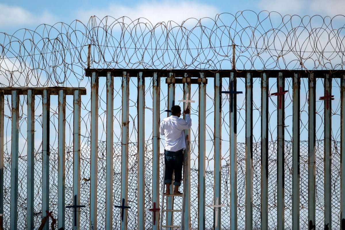 TOPSHOT - Josue Serrano, a Mexican deported migrant, hangs wooden crosses on the border fence as part of a vigil for migrants who died while migrating to the United States, at the US-Mexico border in playas de Tijuana, Baja California state, Mexico, on July 4, 2022. - On June 27, 2022, 53 migrants from Mexico, Guatemala and Honduras were found death abandoned in a suffocatingly hot tractor-trailer truck in the US state of Texas. (Photo by Guillermo Arias / AFP) (Photo by GUILLERMO ARIAS/AFP via Getty Images) (Getty Images)