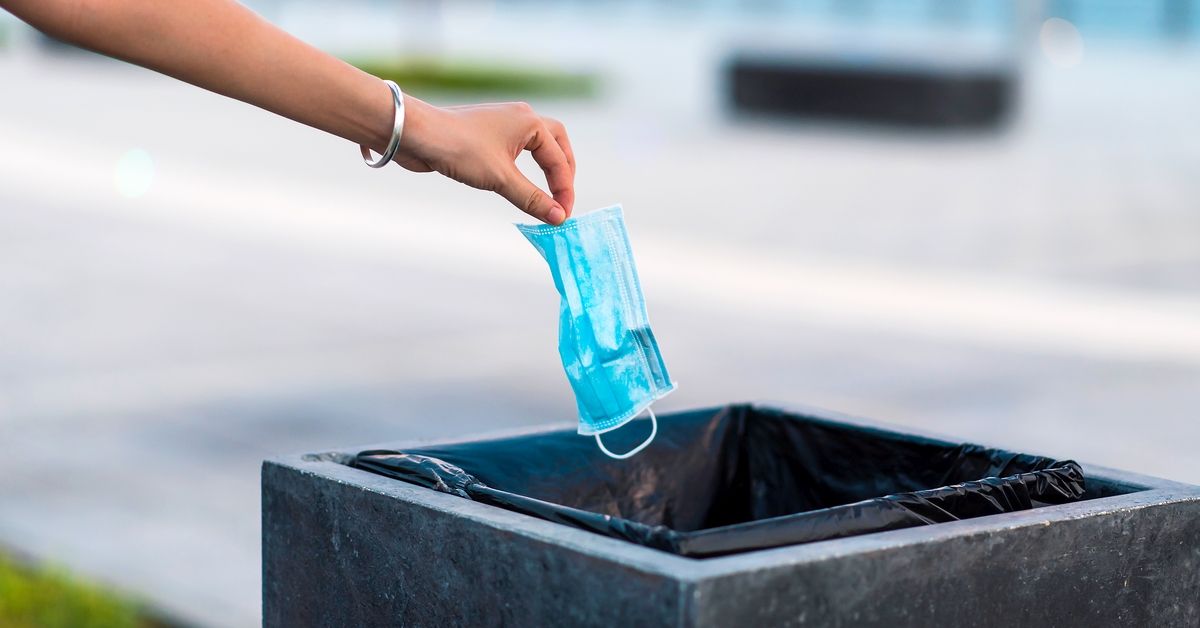 Woman throwing used protective surgical mask into the garbage bin. Close up of a hand that throws the used mask in the public trash can outdoors (Getty Images/Stock photo)
