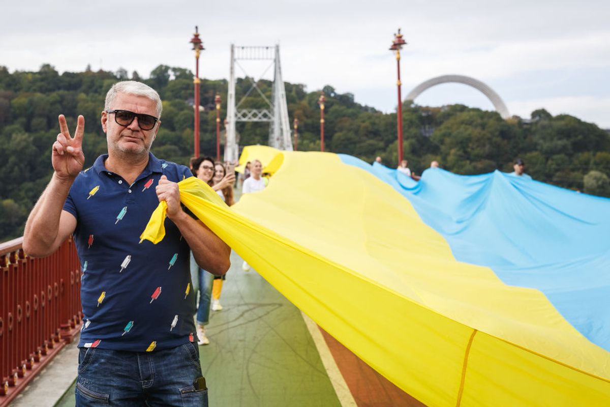 KYIV, UKRAINE - AUGUST 28: A man giving a victory sign holds a 430-meter-long Ukrainian flag along the park pedestrian bridge over the Dnipro River during the “Ukraine is united” political performance on August 28, 2022 in Kyiv, Ukraine. The symbolic unification of the left and right banks of the Dnipro demonstrates the unity of the Ukrainian people in the struggle for Ukraine’s independence. Refugees from the temporarily occupied by Russian forces Ukrainian cities, such as Kherson, Mariupol, Melitopol and others joined the action. On August 23, Ukraine celebrates Day of the National Flag and on August 24 its 1991 declaration of independence from the USSR. The date also marks six months since Russia launched its large-scale invasion of Ukraine. For security reasons and due to the threat of Russian missile strikes on Kyiv the action runs after holidays. (Photo by Yurii Stefanyak/Global Images Ukraine via Getty Images) (Getty Images)