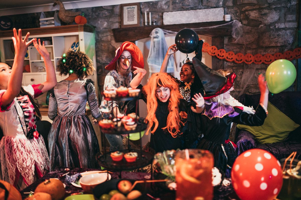 Group of young friends dressed in costumes dancing and playing together at a Halloween party. One of their parents is playing alongside them, also dressed in a costume.