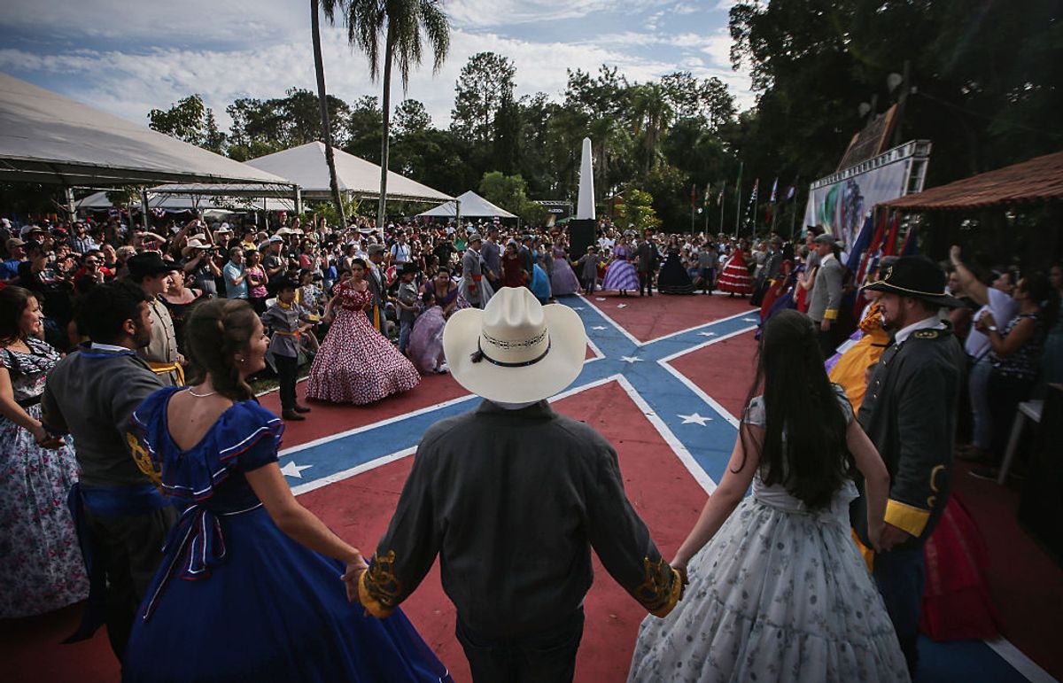 SANTA BARBARA D'OESTE, BRAZIL - APRIL 24: People in traditional outfits hold hands between dances at the annual Festa Confederada, or Confederate Party, on April 24, 2016 in Santa Barbara d'Oeste, Brazil. The festival is put on by Brazilian descendants of families who fled from the southern United States to Brazil during Reconstruction, between 1865 and 1875, following the end of the U.S. Civil War. Thousands attend the festival which is held at the American Cemetery, or Cemiterio dos Americanos, where graves of settlers and descendants remain to this day. The festival features traditional Southern-style dancing, music and cuisine. The U.S. settlers eventually assimilated with local Brazilians and some now are racially mixed while many others no longer speak English. Organizers say the festival represents familial tradition, ancestral heritage and happiness and is not associated with the negative connotations of the Confederacy. The flag carries no stigma or political meaning in Brazil. (Photo by Mario Tama/Getty Images) (Mario Tama/Getty Images)