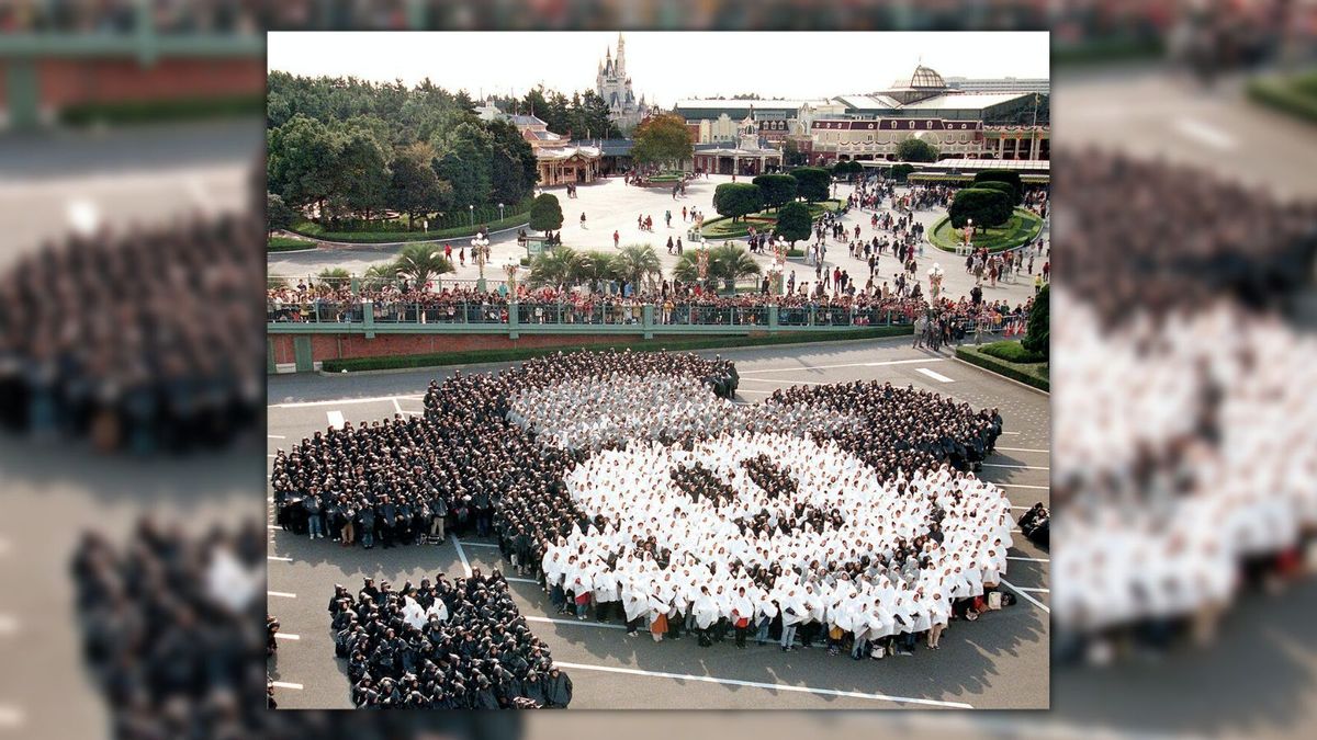 Some 2,300 guests wearing black, gray and white rain coats stand together to form the face of Mickey Mouse to celebrate the famous Disney character's 70th birthday at the parking lot of Tokyo Disneyland in Urayasu, in suburban Tokyo on Nov. 19,1998. (YOSHIKAZU TSUNO/AFP via Getty Images)
