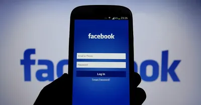 A phone shows Facebook's login page in front of a backdrop that says Facebook on it in blue. 