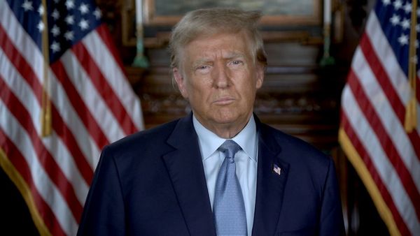 A white man wearing a blue suit looks at a camera.