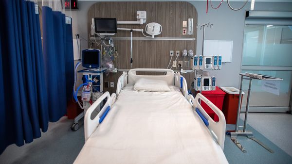 A hospital room is shown. Blue curtains are to the left, while various medical devices are shown in the room. 